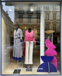 Vitrine Devernois avec silhouettes graphiques colorées en rose et bleu, mannequins habillés et mise en scène contemporaine visible depuis la rue